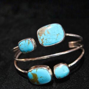 Sterling silver cuff bracelet featuring four natural turquoise stones with golden matrix detailing, displayed on a black background. turquoise 4-stone bracelet